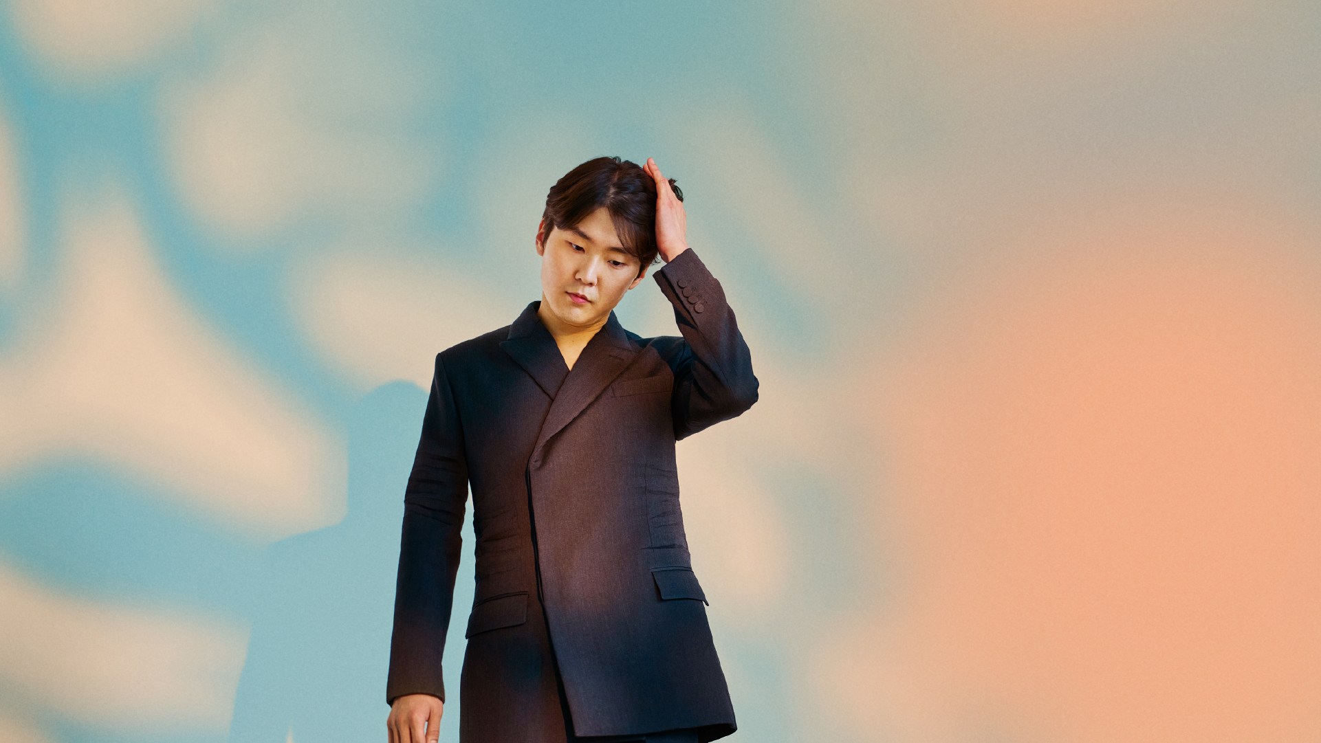 피아니스트 조성진이 푸르고 붉은 배경 중앙에서 머리를 쓸어넘기고 있다.